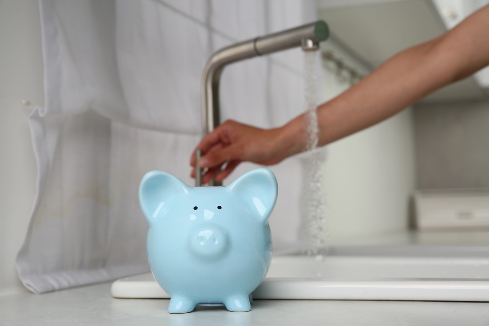 Image of a woman checking water flow in a kitchen, symbolizing a water-saving concept, featuring Knee Deep Plumbing and highlighting concerns about the water bill.